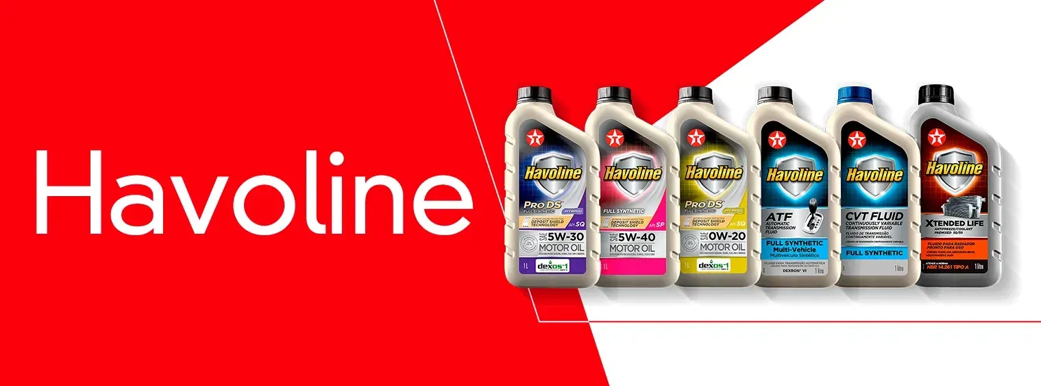 Um homem de macacão amarelo segura um pneu na frente de um carro.