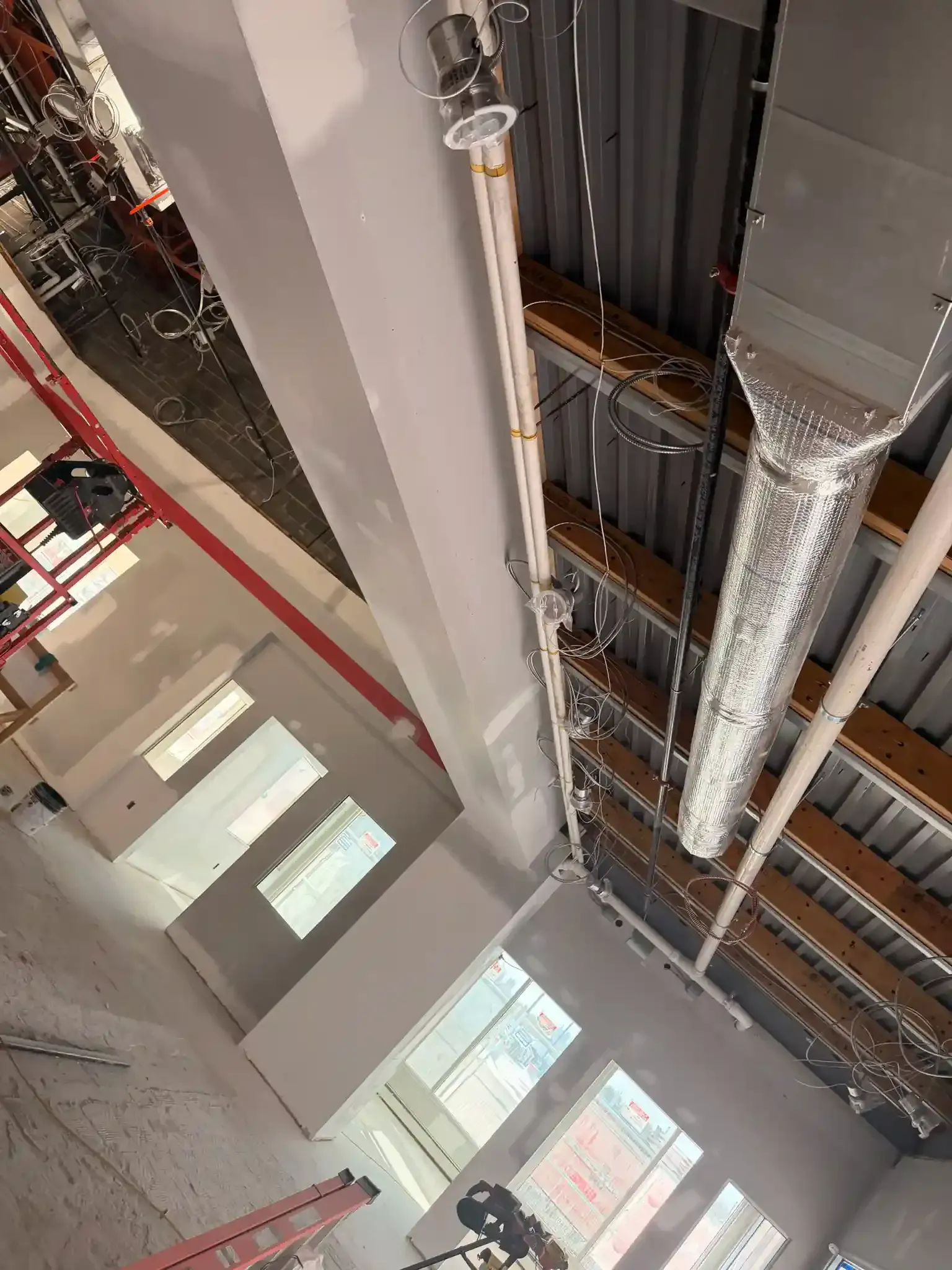 Indoor construction site with exposed ceiling ducts, metal framing, and windows below.