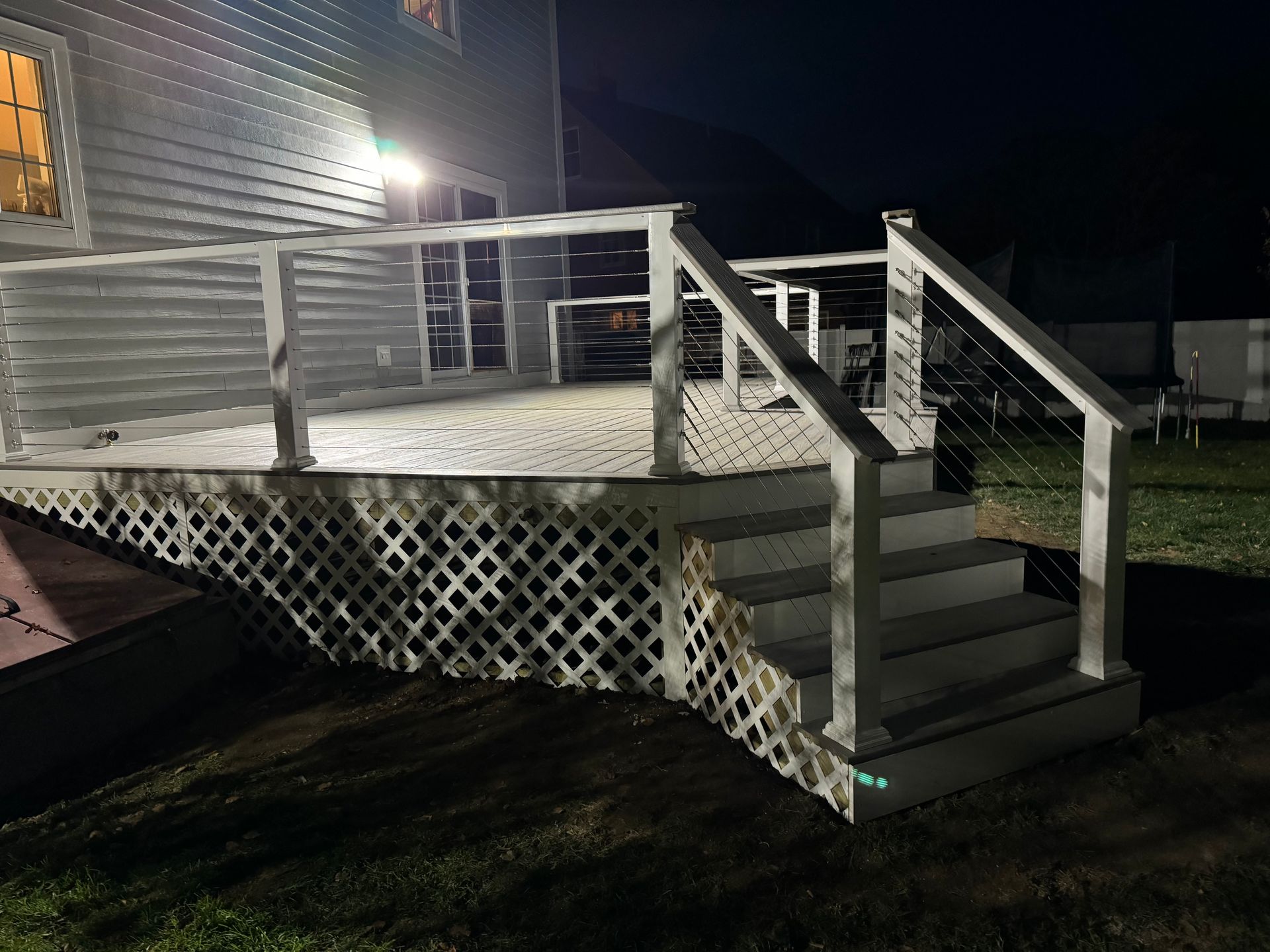 A white deck with stairs leading up to it is lit up at night.