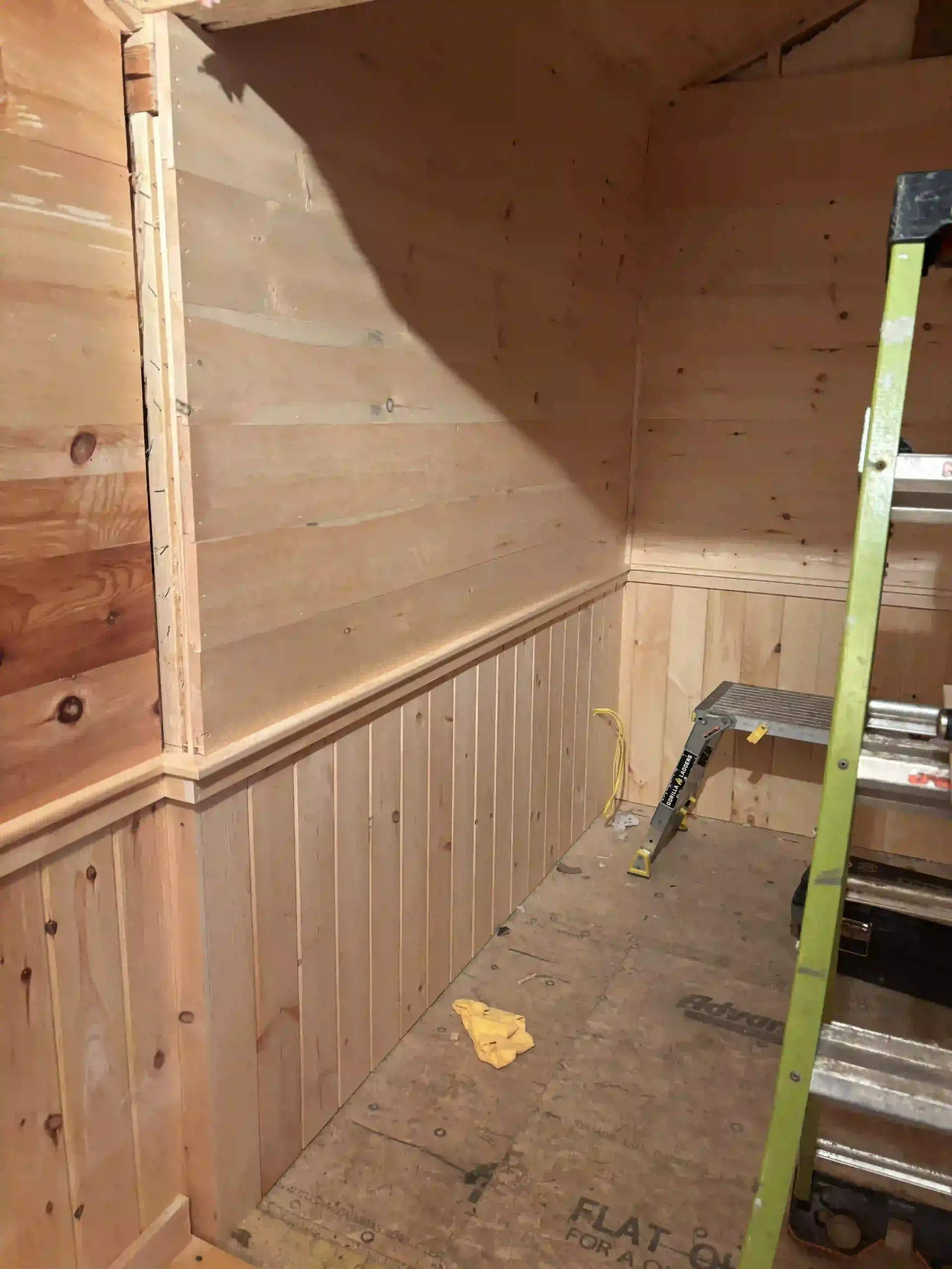 Wood-paneled interior with a ladder against the wall and a concrete floor in a small room
