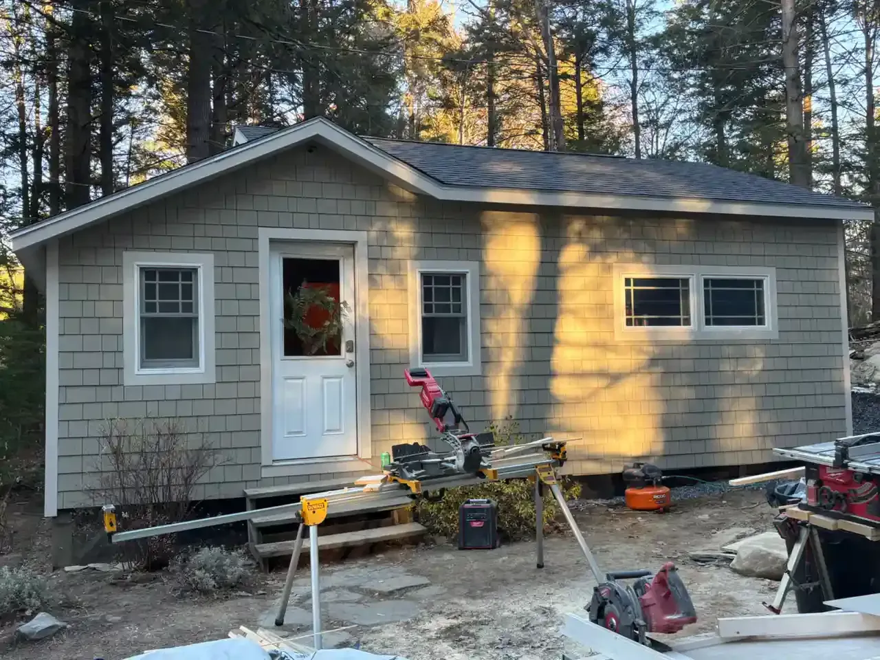 Small gray house under construction with tools and materials scattered in the yard.