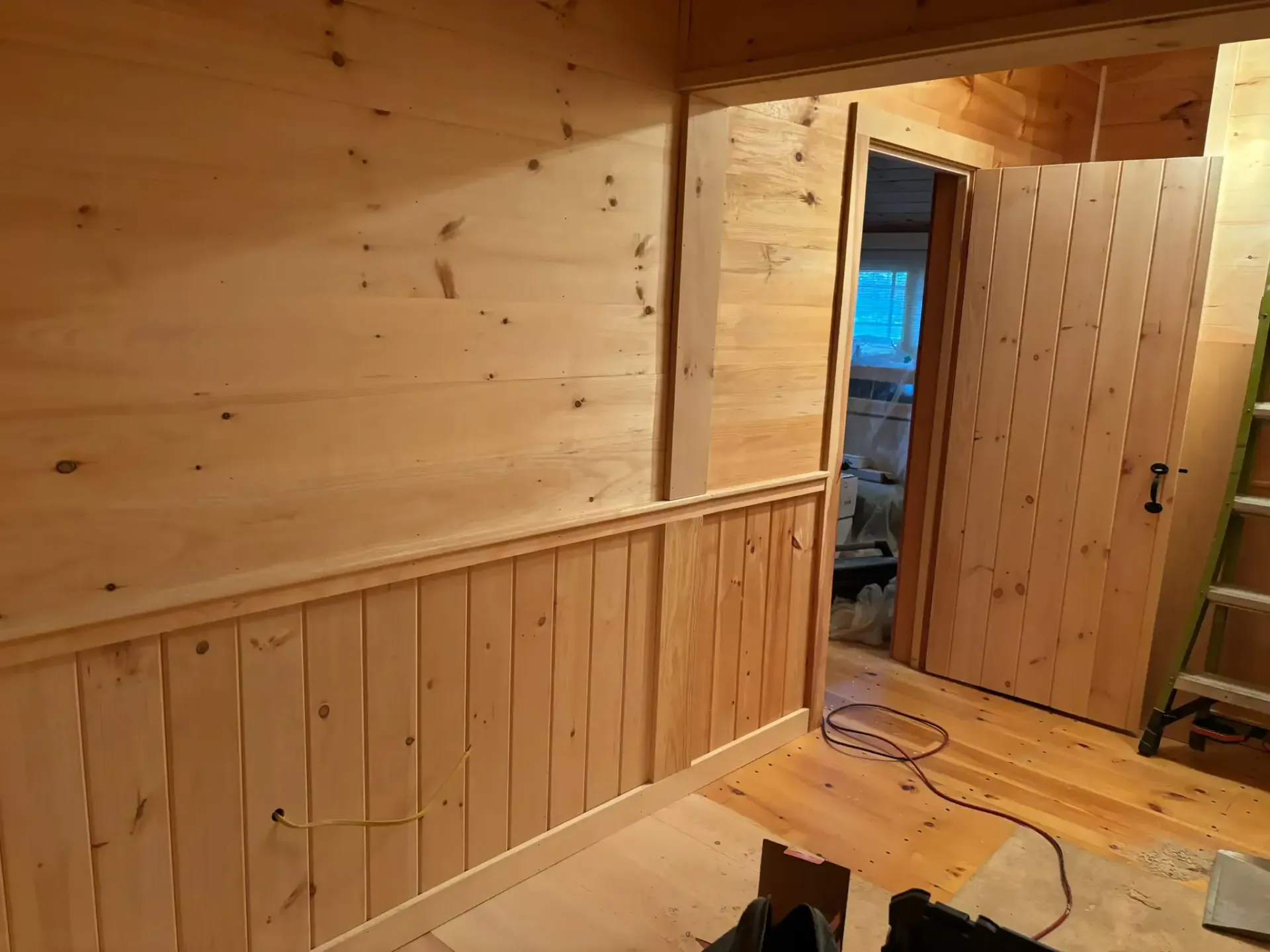 Wood-paneled cabin hallway with an open door, blue light beyond, and a black cat on the wooden floor