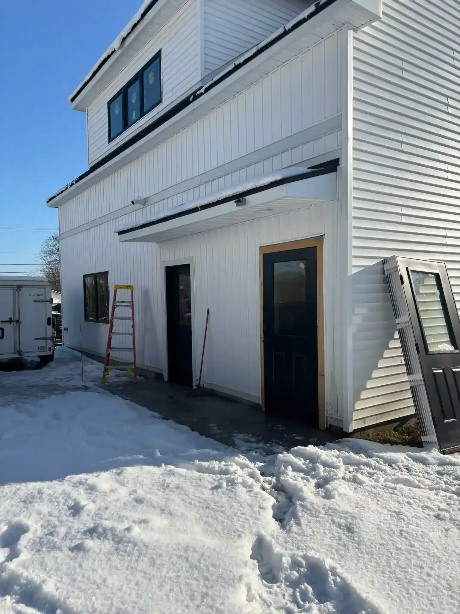 Snowy side view of a white building with two doors and an exterior staircase