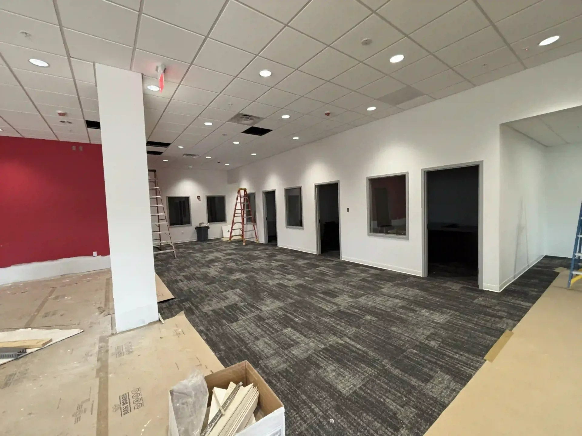 Empty office interior with carpet, white columns, red accent wall, and multiple open doorways