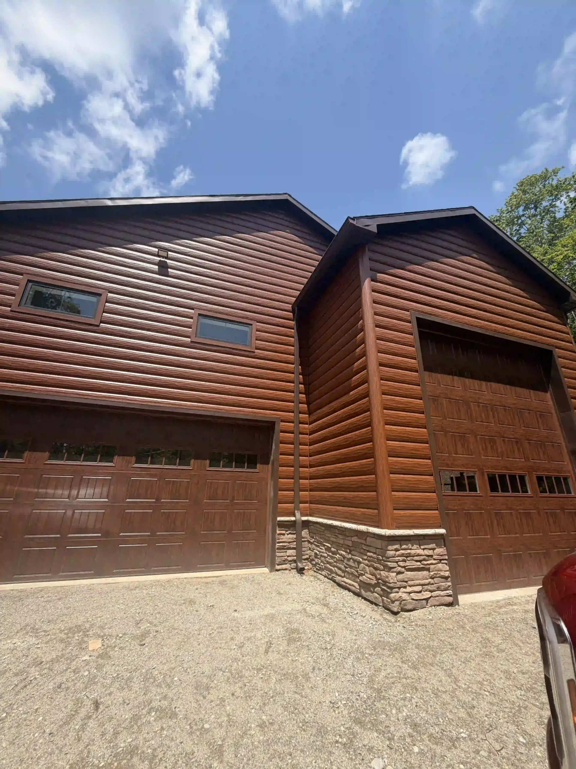 Log cabin-style house with brown garage door, stone base, and blue sky above