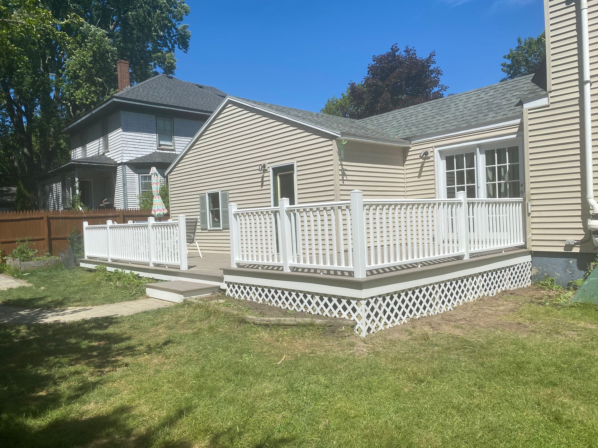 A white deck with a white railing is in the backyard of a house.