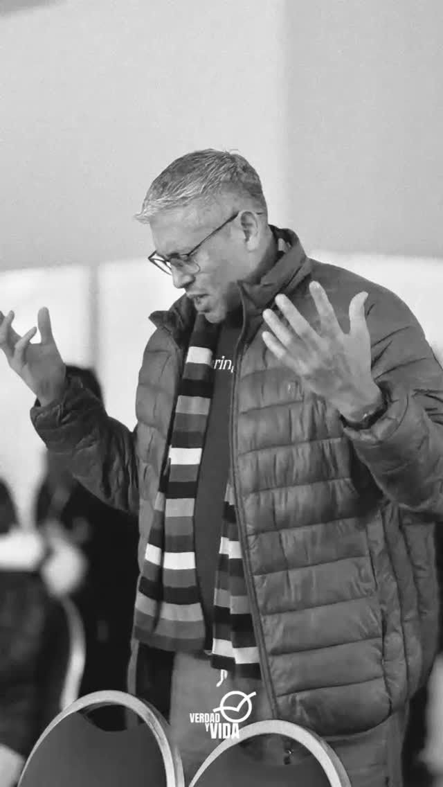 Hombre de pelo gris, vestido con chaqueta y bufanda, gesticula con las manos abiertas, en interiores.