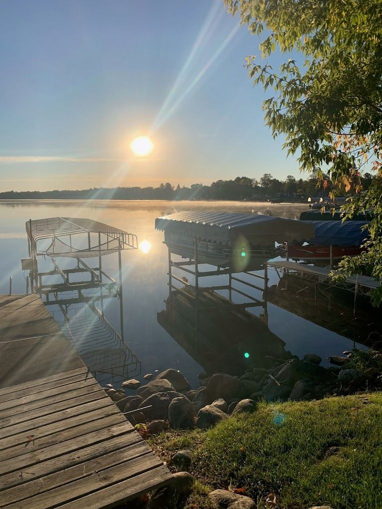 The sun is setting over a lake with a dock in the foreground.