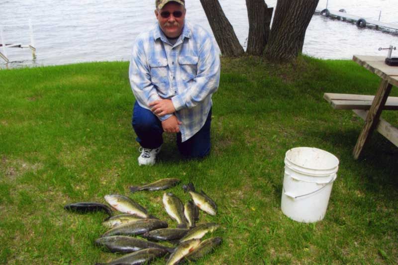 A man is kneeling down next to a pile of fish.