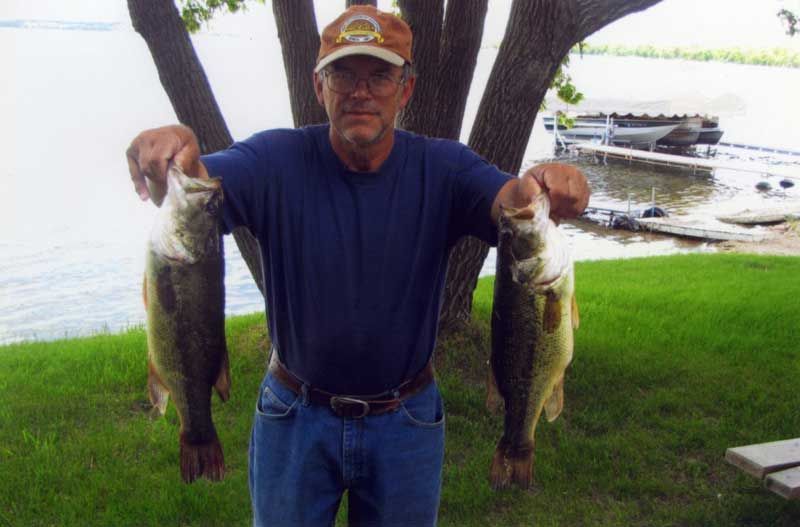 A man is holding two fish in his hands in front of a body of water.