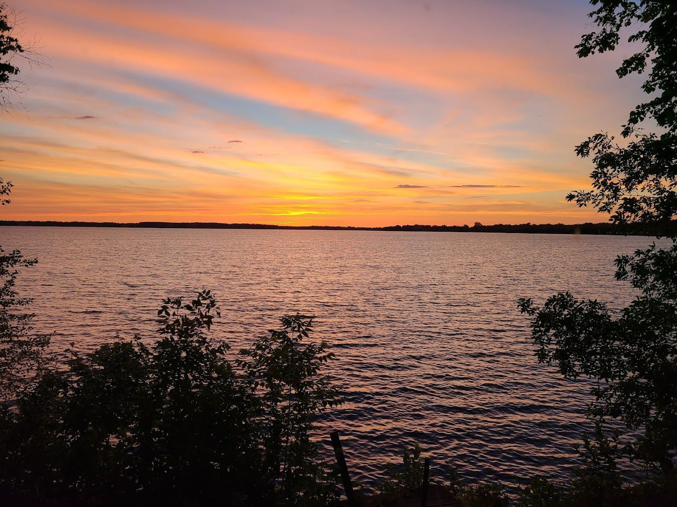 A sunset over a large body of water with trees in the foreground