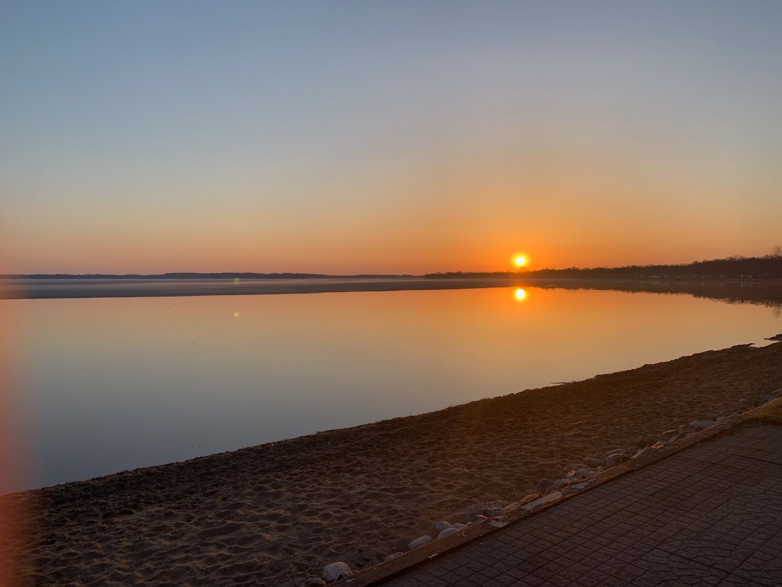 A man is standing on a paddle board in the ocean at sunset.