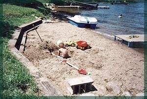 A child is playing in a sandbox next to a body of water.