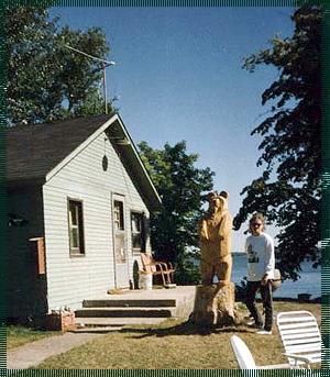 A man is standing in front of a house with a statue of a bear on a stump.