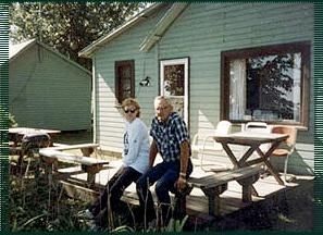 A man and a woman are sitting on a picnic table in front of a house.