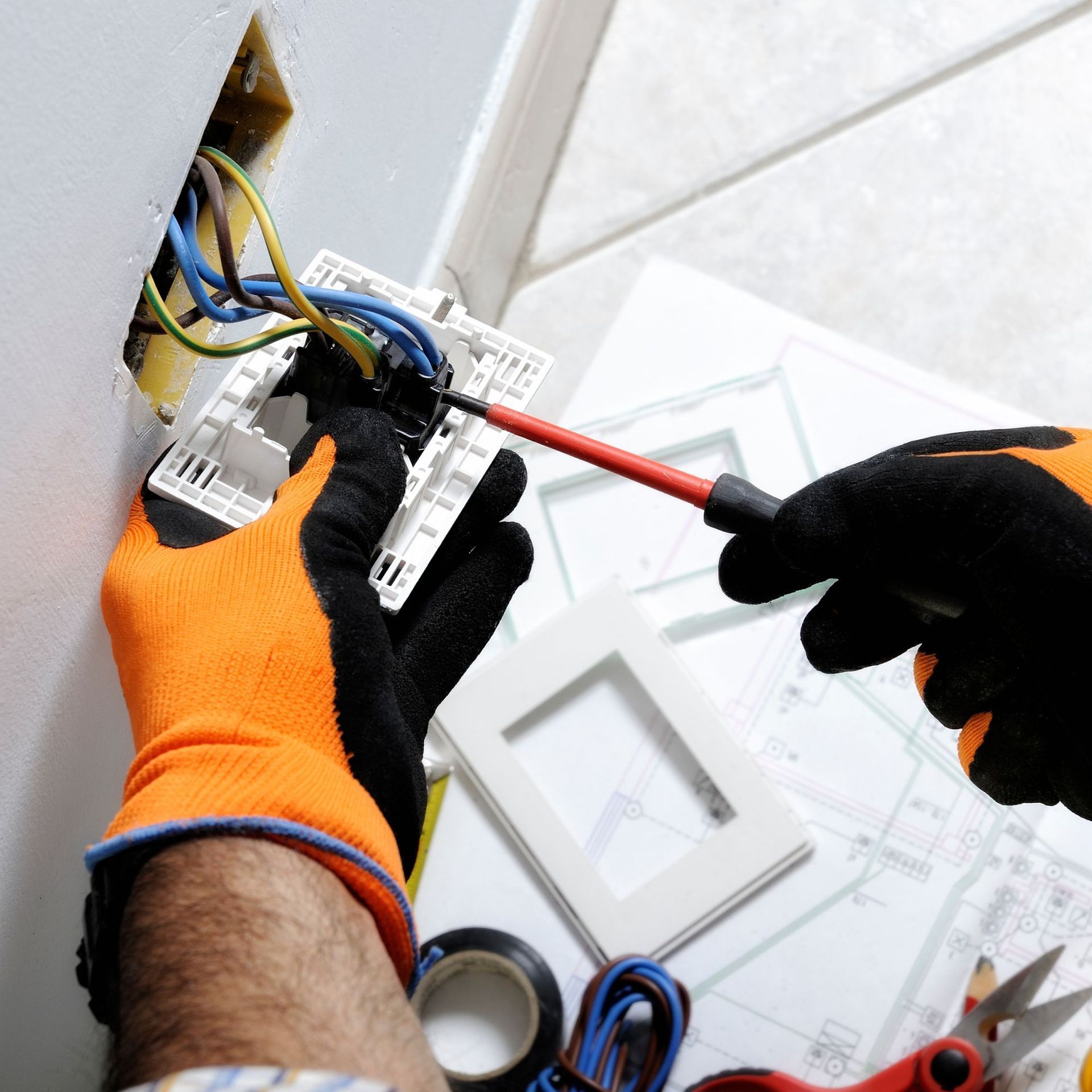 Freedom Electric Construction - A person wearing orange gloves is working on an electrical outlet