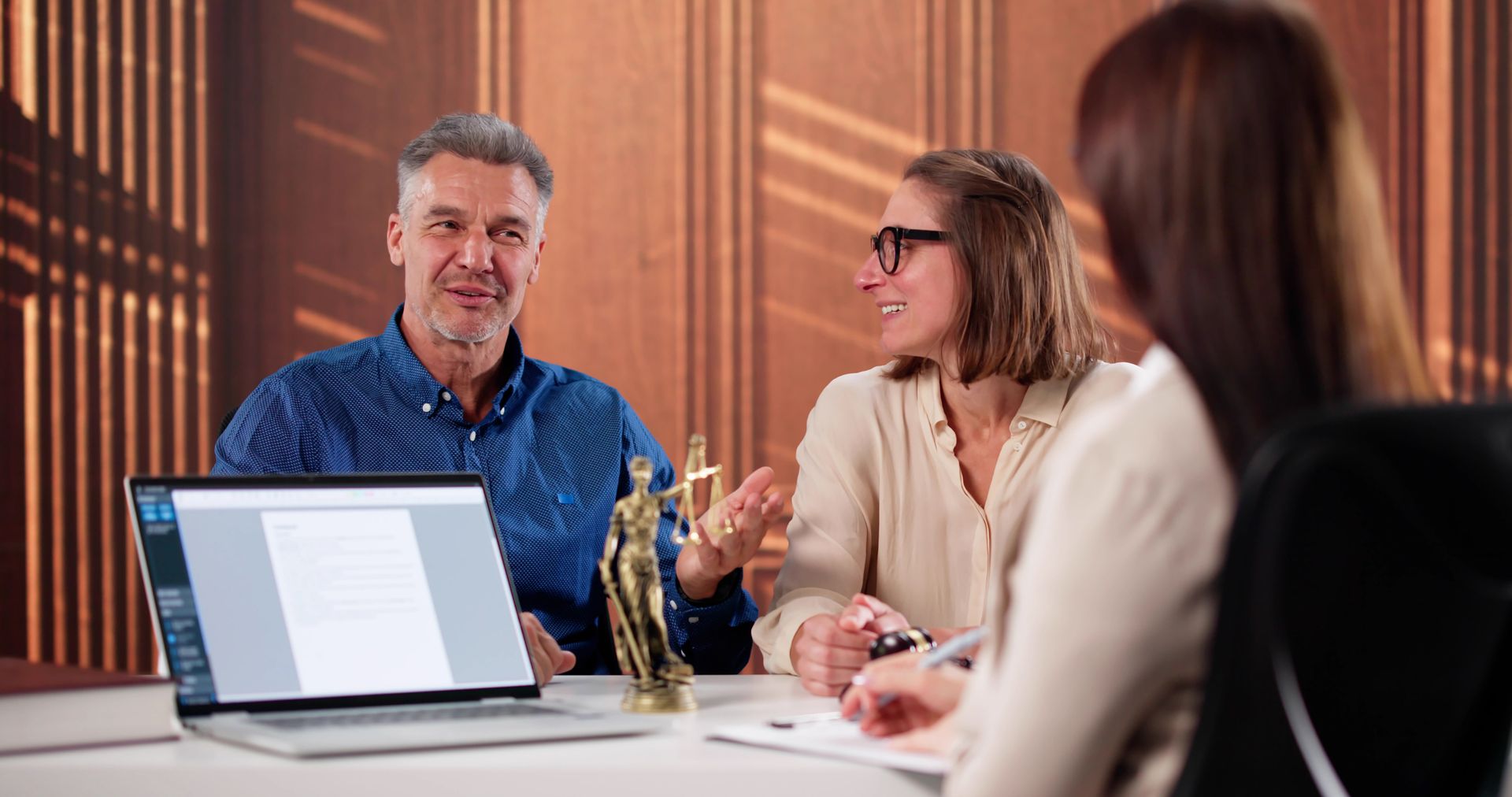 Two clients consult an estate planning lawyer with a Lady Justice statue in the office.