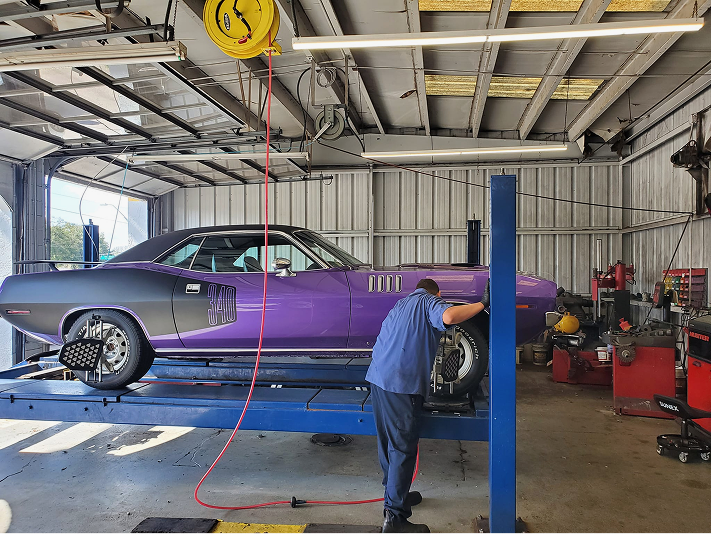 A mechanic adjusting the front wheel of a purple classic car on a lift inside a garage. | A+ Brakes & Suspension