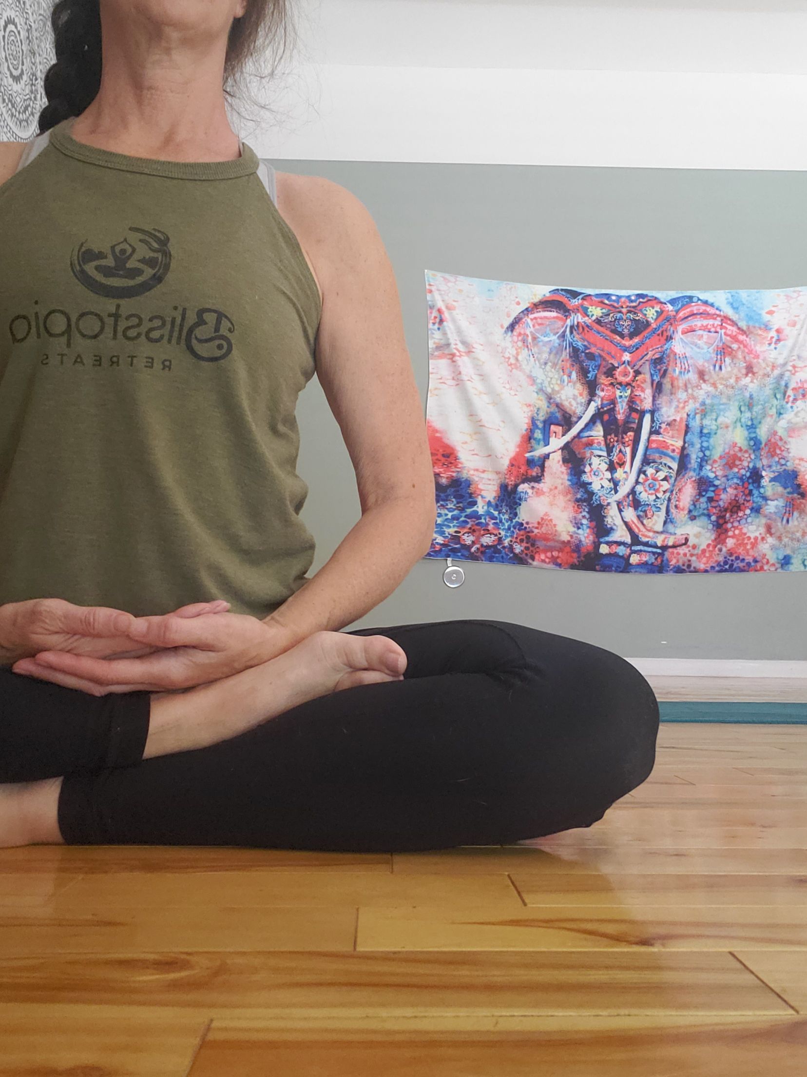 Yoga class with instructor adjusting a student's posture, others in meditation pose, indoor gym setting.