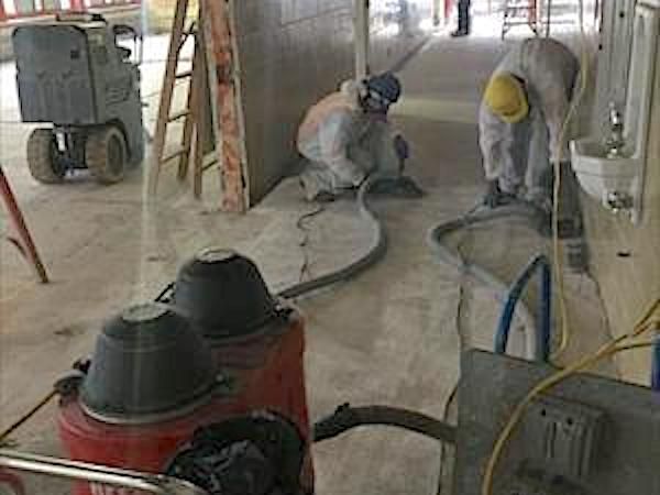 Workers in protective suits removing something from a floor, with equipment present.