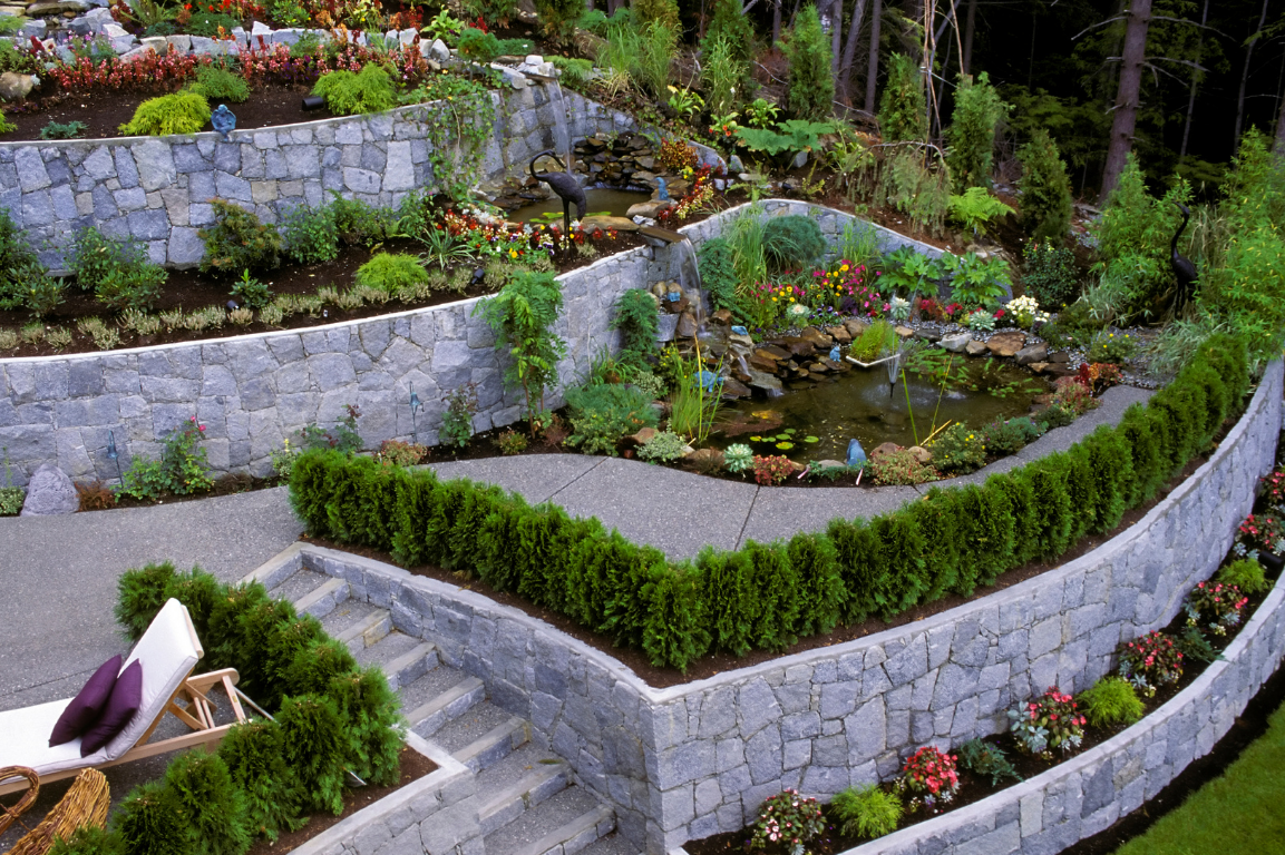 Tiered stone retaining walls with decorative plants and a water feature in a beautifully designed Redmond landscape