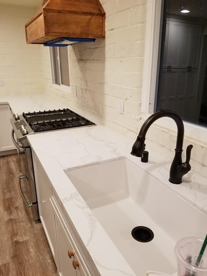 Kitchen with white countertops, brick JJR Construction -  backsplash, gas stove, farmhouse sink, and dark faucet.