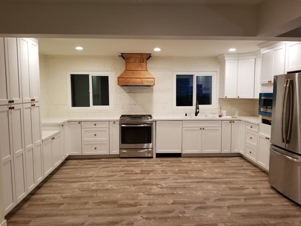 JJR Construction -  White kitchen with stainless steel appliances, copper range hood, and wood-look flooring.