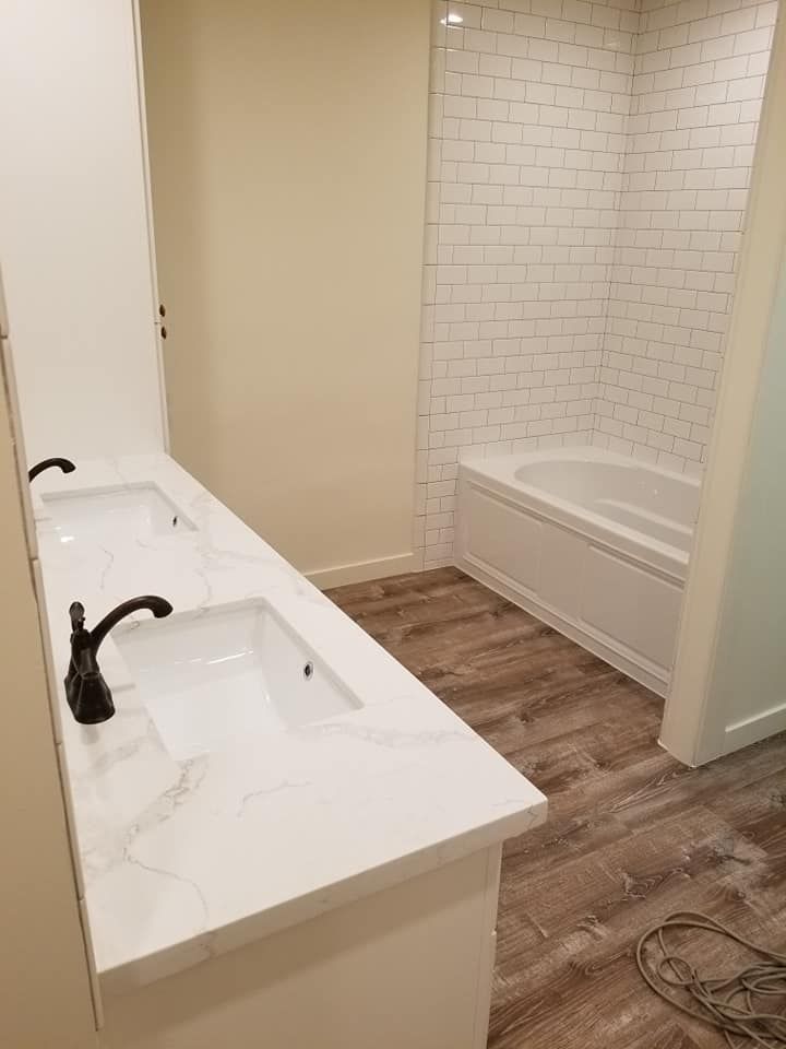 JJR Construction - Bathroom with a white double vanity, black faucets, and a bathtub with white subway tile.