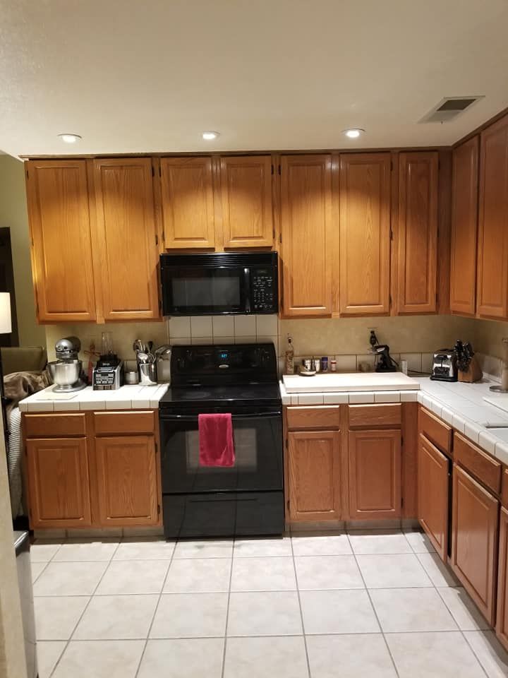 JJR Construction -  A kitchen with light brown cabinets, white counters and floor, and a black stove and microwave.