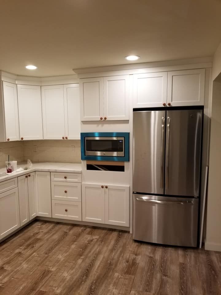 JJR Construction -  White kitchen with stainless steel fridge, microwave in turquoise frame, and wood-look flooring.