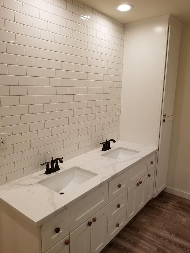 JJR Construction -  White bathroom with double vanity, marble countertop, and tiled backsplash. Dark faucets.
