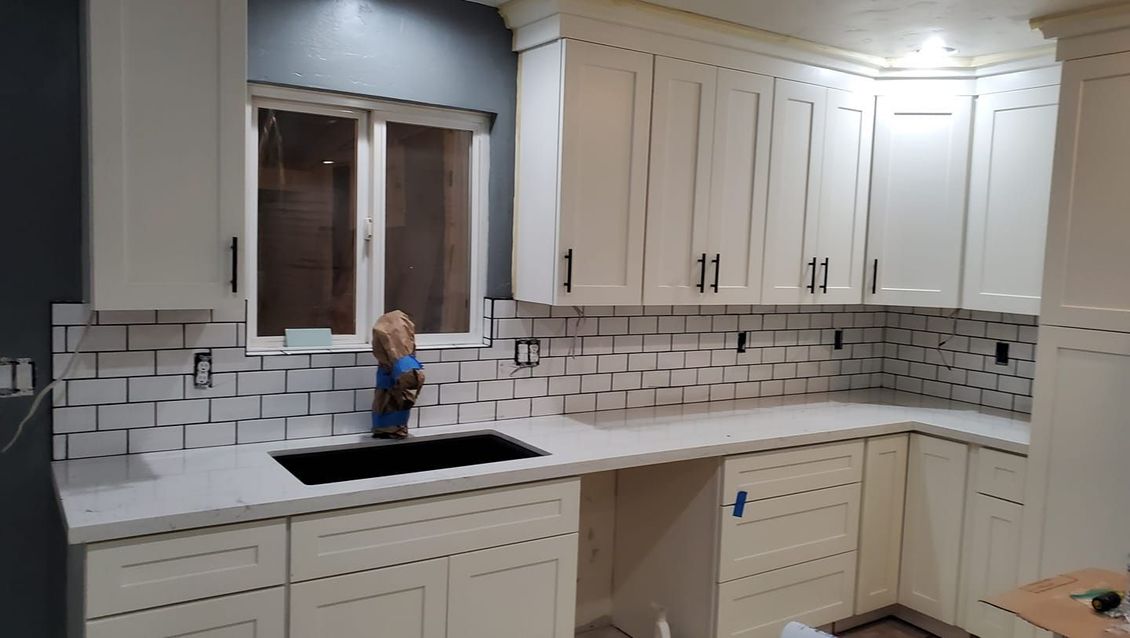 JJR Construction -  Cream kitchen with white countertop, black sink, and subway tile backsplash.