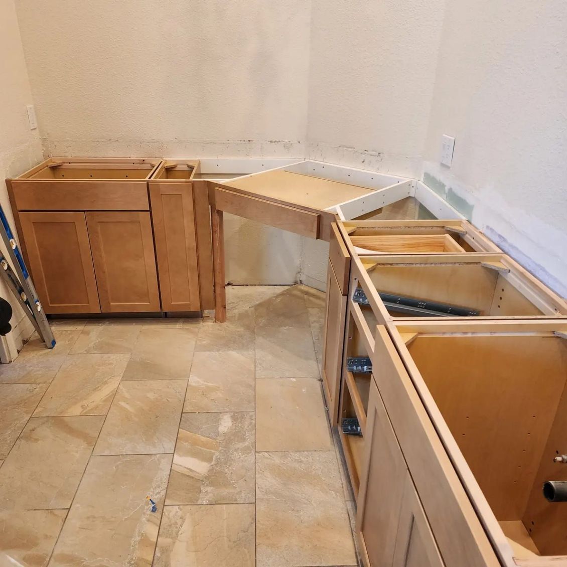 Kitchen cabinets in various stages of assembly, with light-colored wood and tan tile flooring.JJR Construction -  