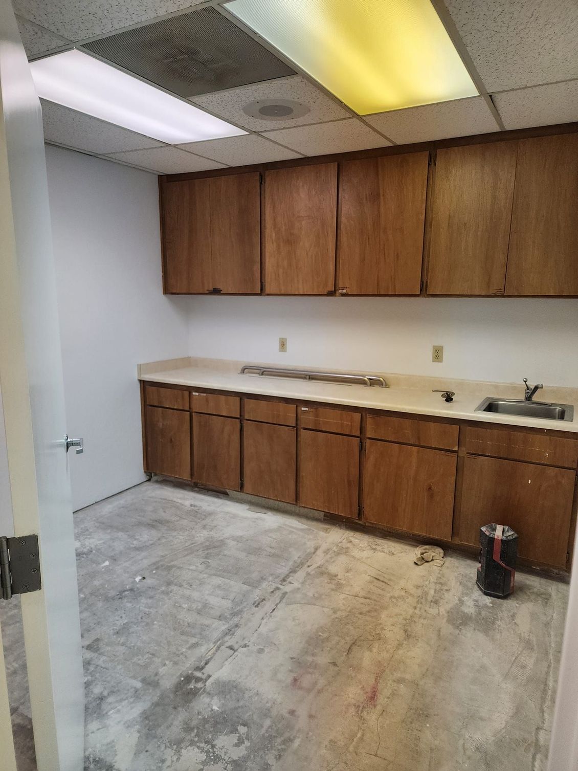 JJR Construction -  A small, empty kitchenette with wood cabinets, a sink, and a stained concrete floor.