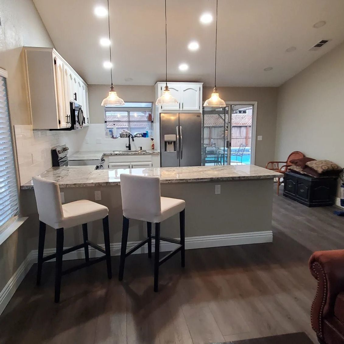 JJR Construction -  Modern kitchen with granite countertops, white cabinets, and a breakfast bar with two stools.