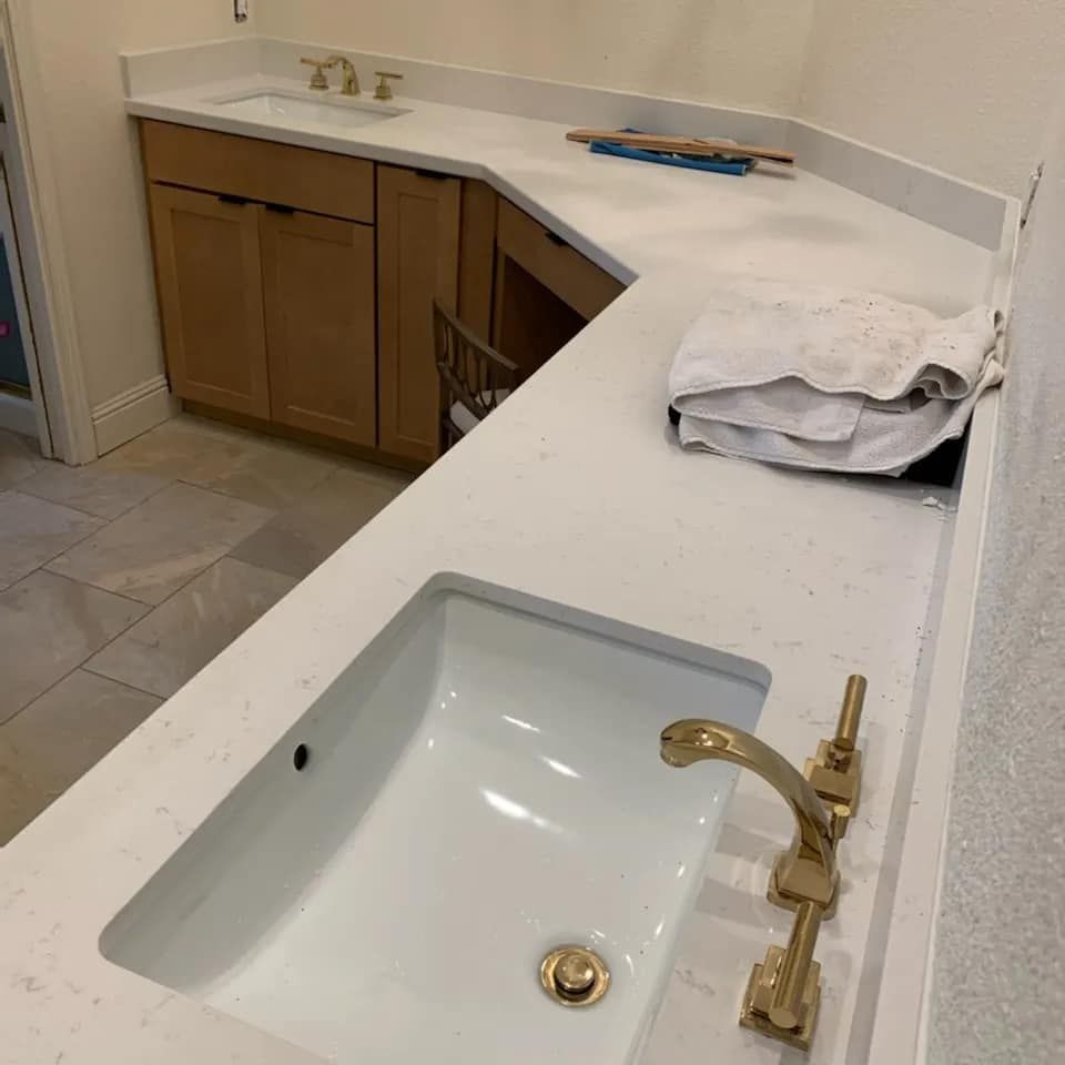 JJR Construction -  Bathroom counter with white sink, gold faucet, and light wood cabinets.