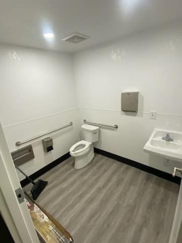 JJR Construction -  An accessible restroom with a toilet, sink, and grab bars. White walls, gray floor, stainless steel.