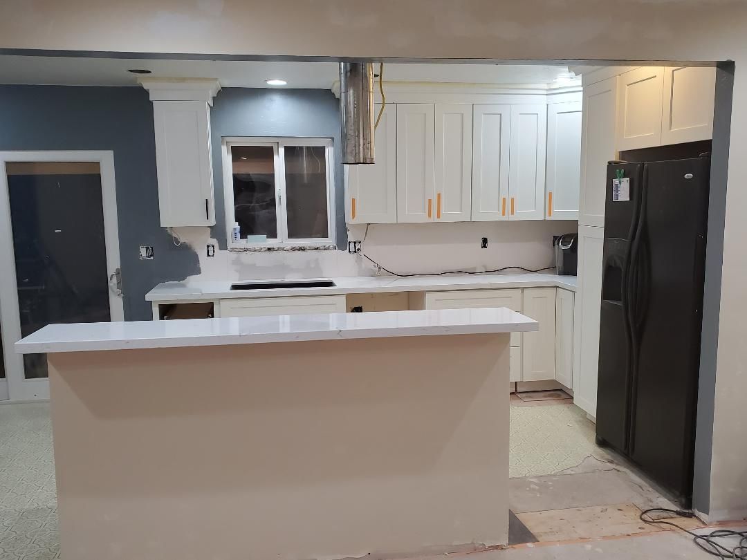 JJR Construction - Kitchen renovation in progress: white cabinets, countertops, and island; black fridge; blue wall.
