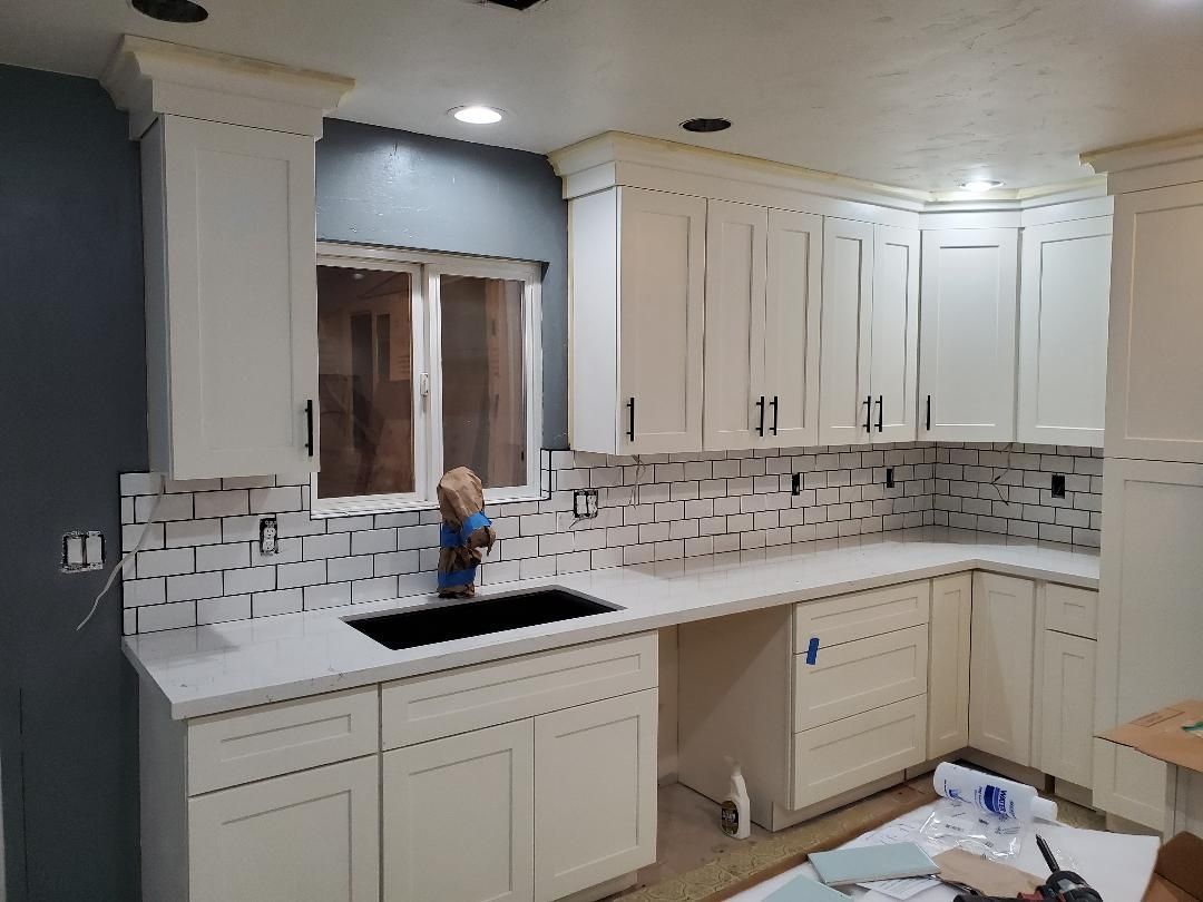 JJR Construction -  White kitchen with cream cabinets, marble backsplash, and dark hardware.