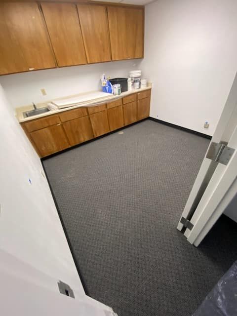 JJR Construction -  Empty room with gray carpet, wood cabinets, and white walls. Includes a sink area.