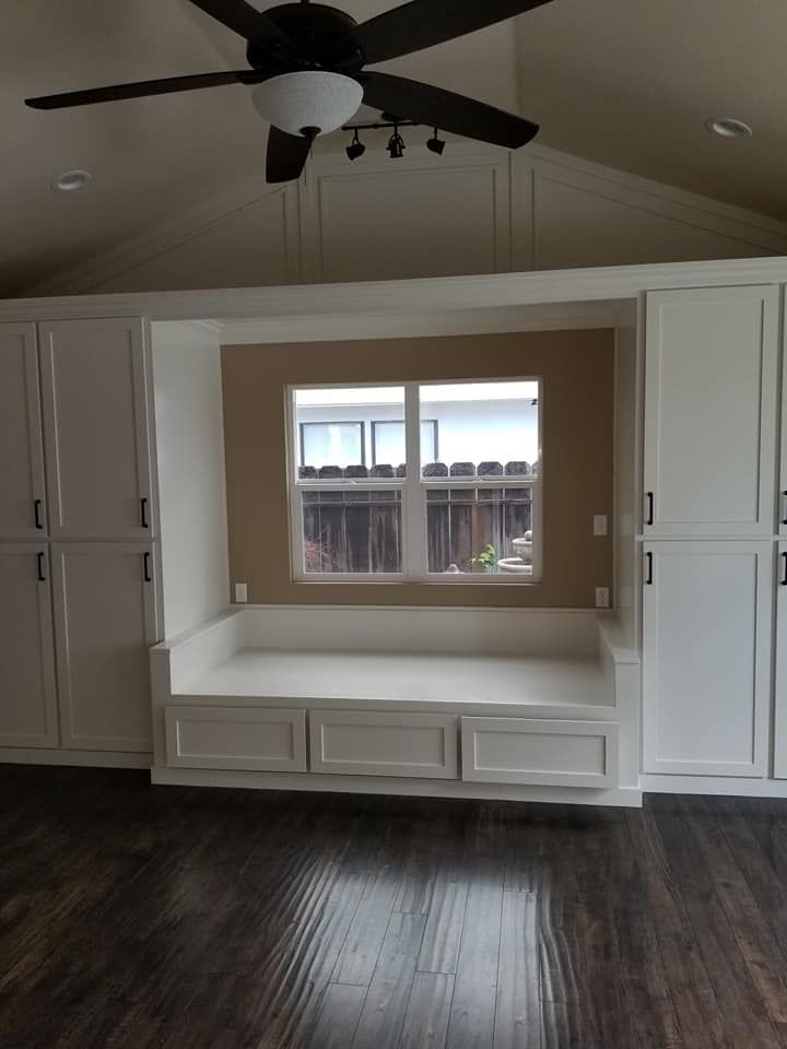 JJR Construction - White cabinetry surrounds a window seat with storage. A dark ceiling fan hangs above dark wood floors.