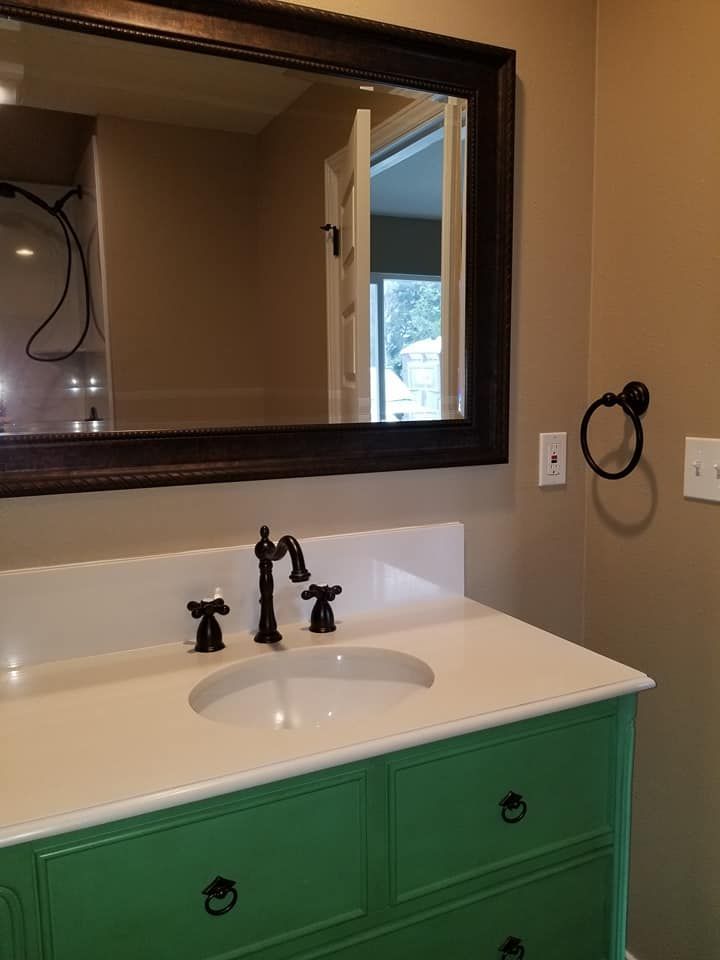 JJR Construction - Green vanity with white countertop, black faucet and fixtures, and a dark framed mirror.