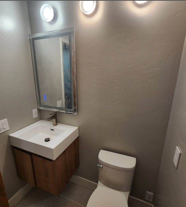 Bathroom with a floating wood vanity, square sink, mirror, and toilet; neutral color walls.
