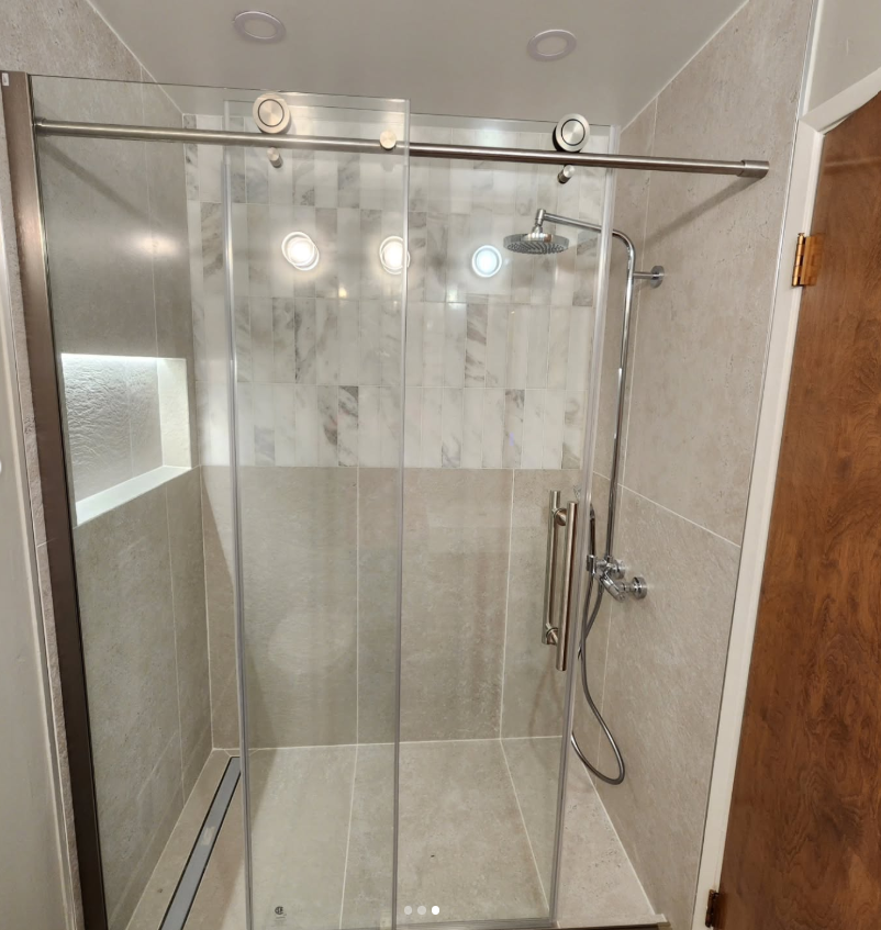 Modern shower with sliding glass doors, stainless steel fixtures, and light gray tiles.