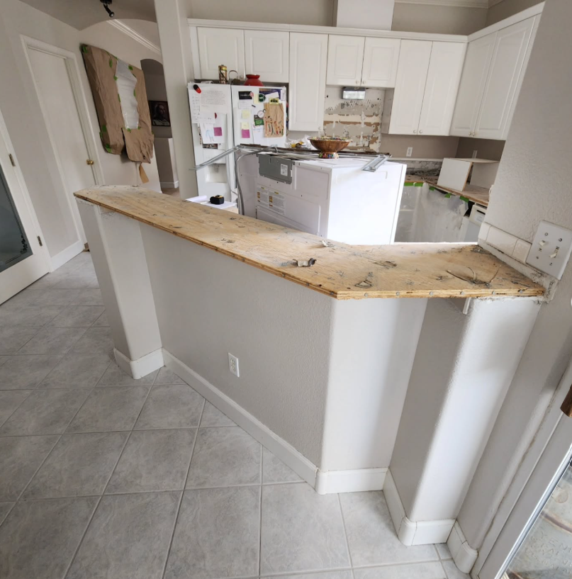 JJR Construction - Kitchen with white cabinets, an island, and gray tile floors undergoing renovation.