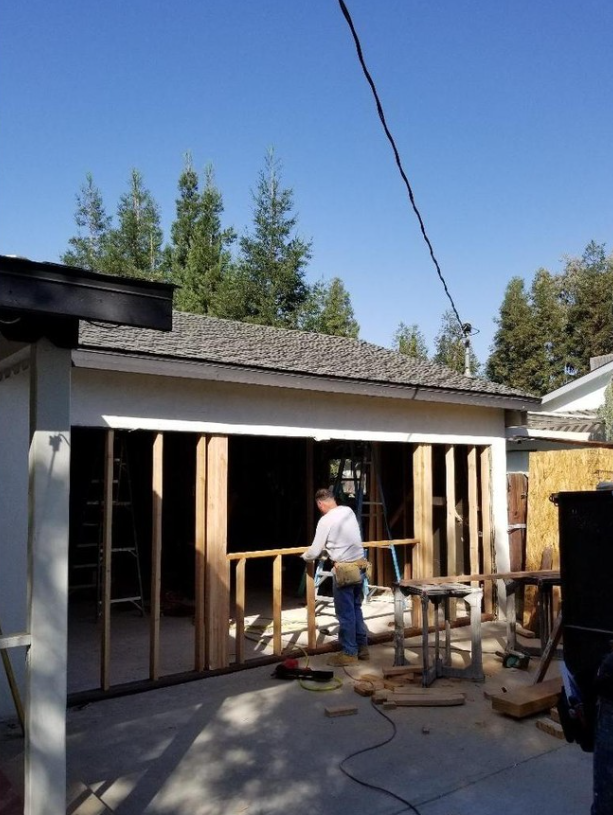 JJR Construction - Man building a wooden frame on a concrete slab outside a building, clear sunny day.