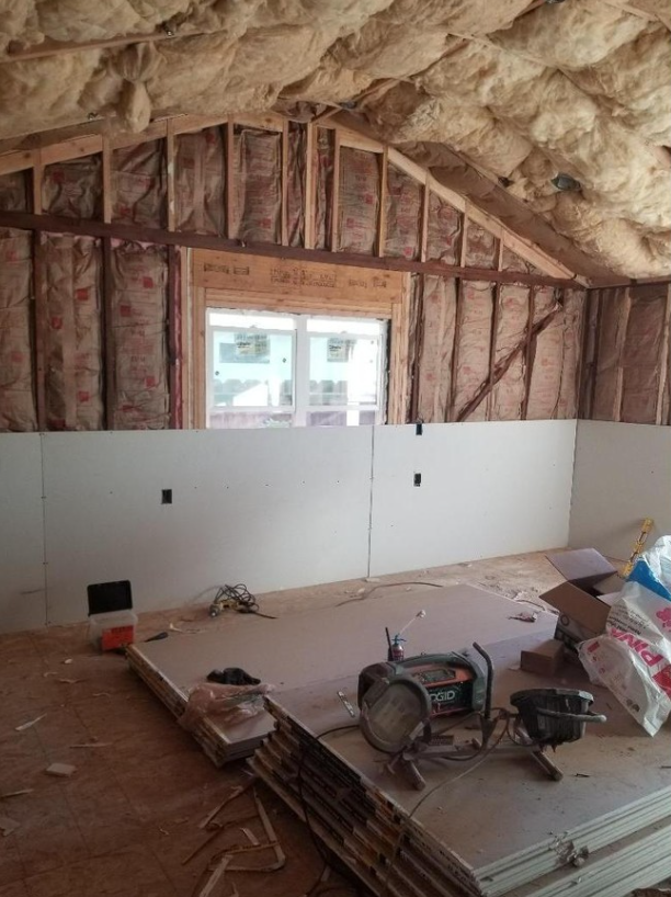 JJR Construction - Interior of a room under construction with insulation, drywall, and tools; window visible.