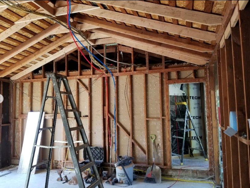 JJR Construction - Construction site interior with exposed wooden framing, ladder, and blue/red pipes.