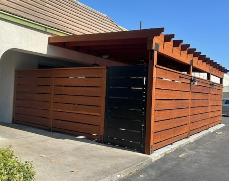 JJR Construction - Wooden fence and pergola attached to a building, with a black gate.