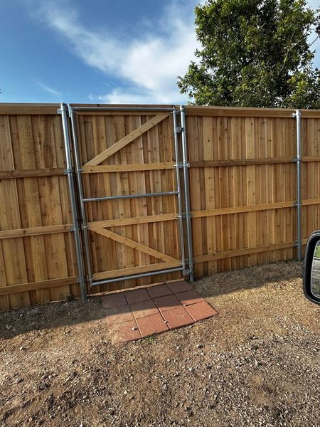 Wooden fence with a gate, made of wood and metal. Red brick path leads to the gate.